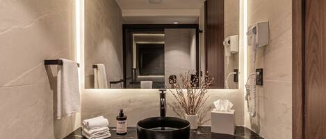 A modern bathroom with a marble countertop, a black vessel sink, a mirror, a towel rack, a plant, and a hand dryer.