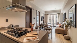 Cozinha moderna com ilha central, área de jantar com mesa redonda e sala de estar com sofá e janelas amplas.