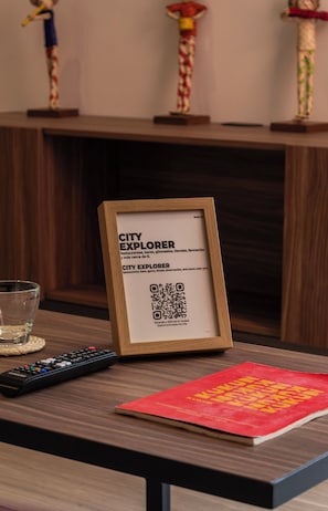 A framed City Explorer sign with a QR code on a wooden table, a remote control, and a red booklet. - LIV Reforma Kukun Apartments  (Ciudad de México)