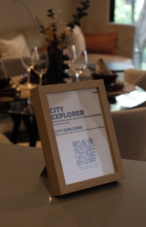 Une plaque « City Explorer » encadrée, avec un code QR, est posée sur une table dans une pièce où se trouvent un canapé et un vase de fleurs.