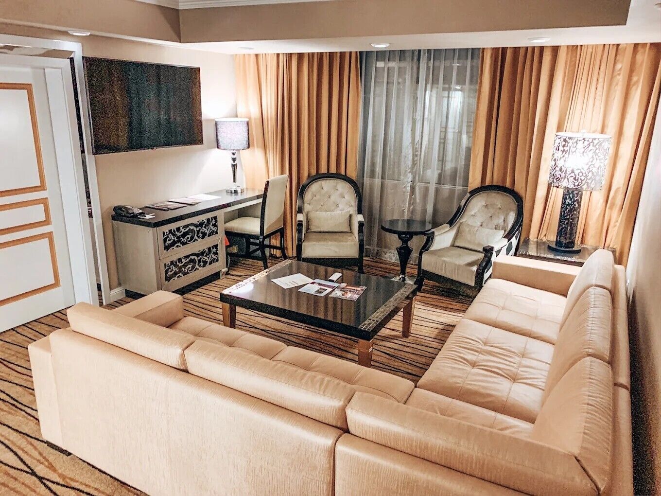 A hotel room with a sofa, armchairs, a coffee table, a desk, and a television.