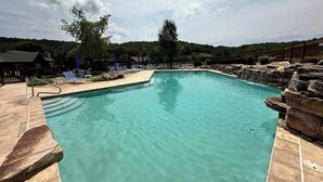 A swimming pool with clear water, surrounded by lounge chairs and a wooden deck. - Teetime Green On the Fairway (Camdenton)