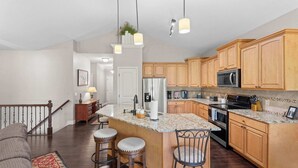 A kitchen with wooden cabinets, granite countertops, stainless steel appliances, and a bar area with stools. - Teetime Green On the Fairway (Camdenton)
