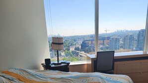 A hotel room with a large window, a bed, a desk, and a lamp.
