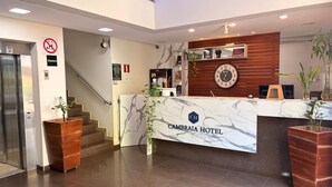 Zona de recepción de un hotel, con un mostrador de mármol, un reloj y una escalera.