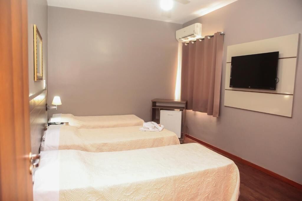 A hotel room with two beds, a TV mounted on the wall, an air conditioning unit, and a small desk with a telephone.