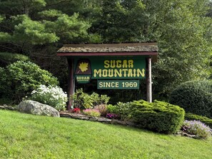 A rustic gazebo with a sign reading 'Sugar Mountain Since 1969' surrounded by lush greenery and flowering plants. - Escape to the Cabin Between the Creeks a 2-bedroom house in Sugar Mountain, NC (Sugar Mountain)