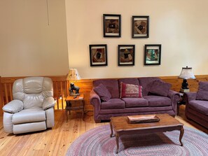 A living room with a leather armchair, a purple sofa, a wooden coffee table, and a rug. - Escape to the Cabin Between the Creeks a 2-bedroom house in Sugar Mountain, NC (Sugar Mountain)