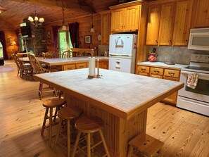 A wooden interior with a kitchen island, bar stools, and a dining area. - Escape to the Cabin Between the Creeks a 2-bedroom house in Sugar Mountain, NC (Sugar Mountain)