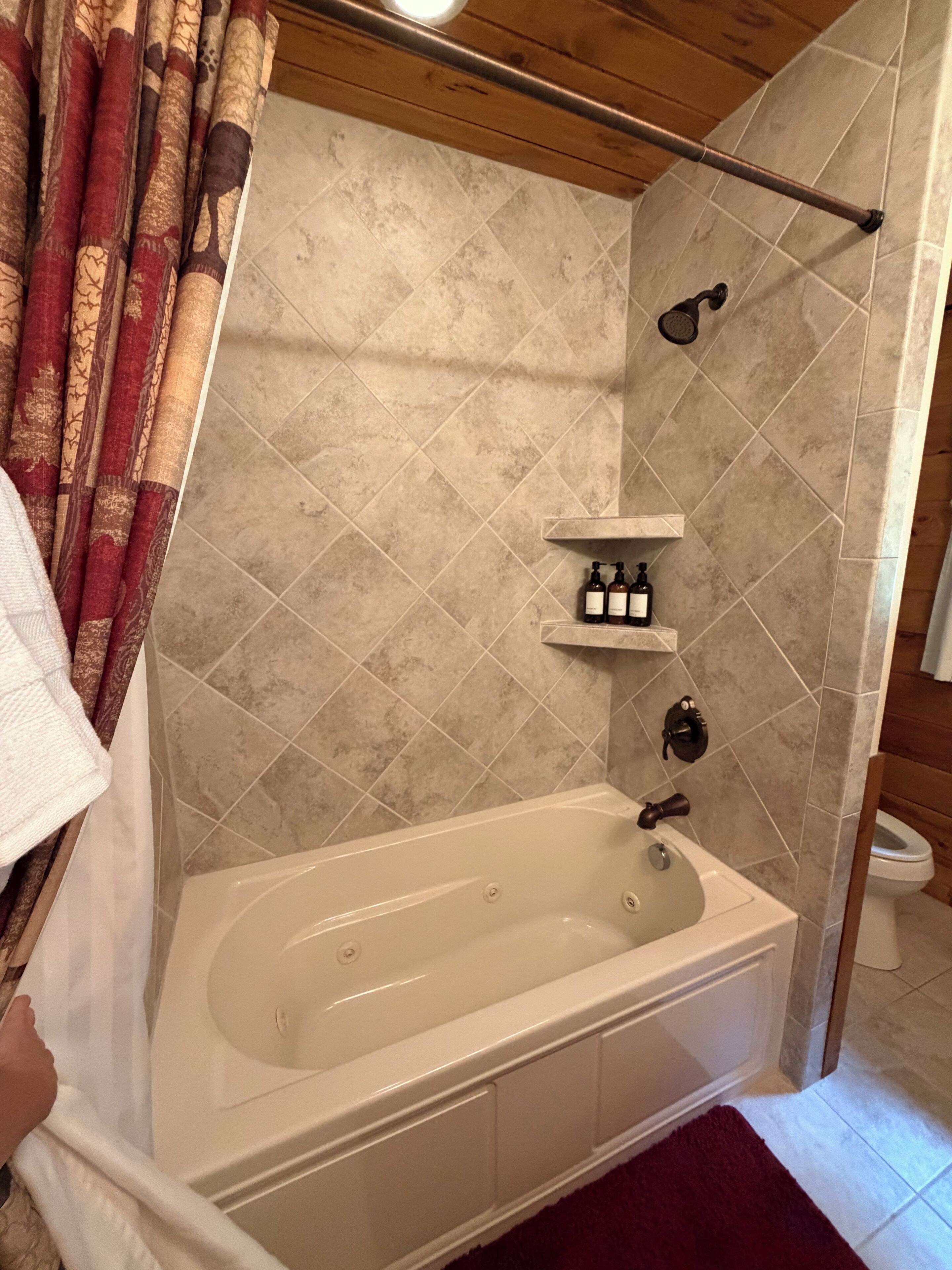 A bathroom with a bathtub, a shower, and a toilet. There are toiletries on a shelf above the bathtub.