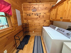 A compact laundry room with wooden walls, a washing machine, and a drying rack. - Escape to the Cabin Between the Creeks a 2-bedroom house in Sugar Mountain, NC (Sugar Mountain)
