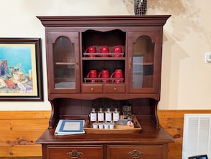 A wooden cabinet with glass doors, red teapots, and a tray with bottles. - Escape to the Cabin Between the Creeks a 2-bedroom house in Sugar Mountain, NC (Sugar Mountain)