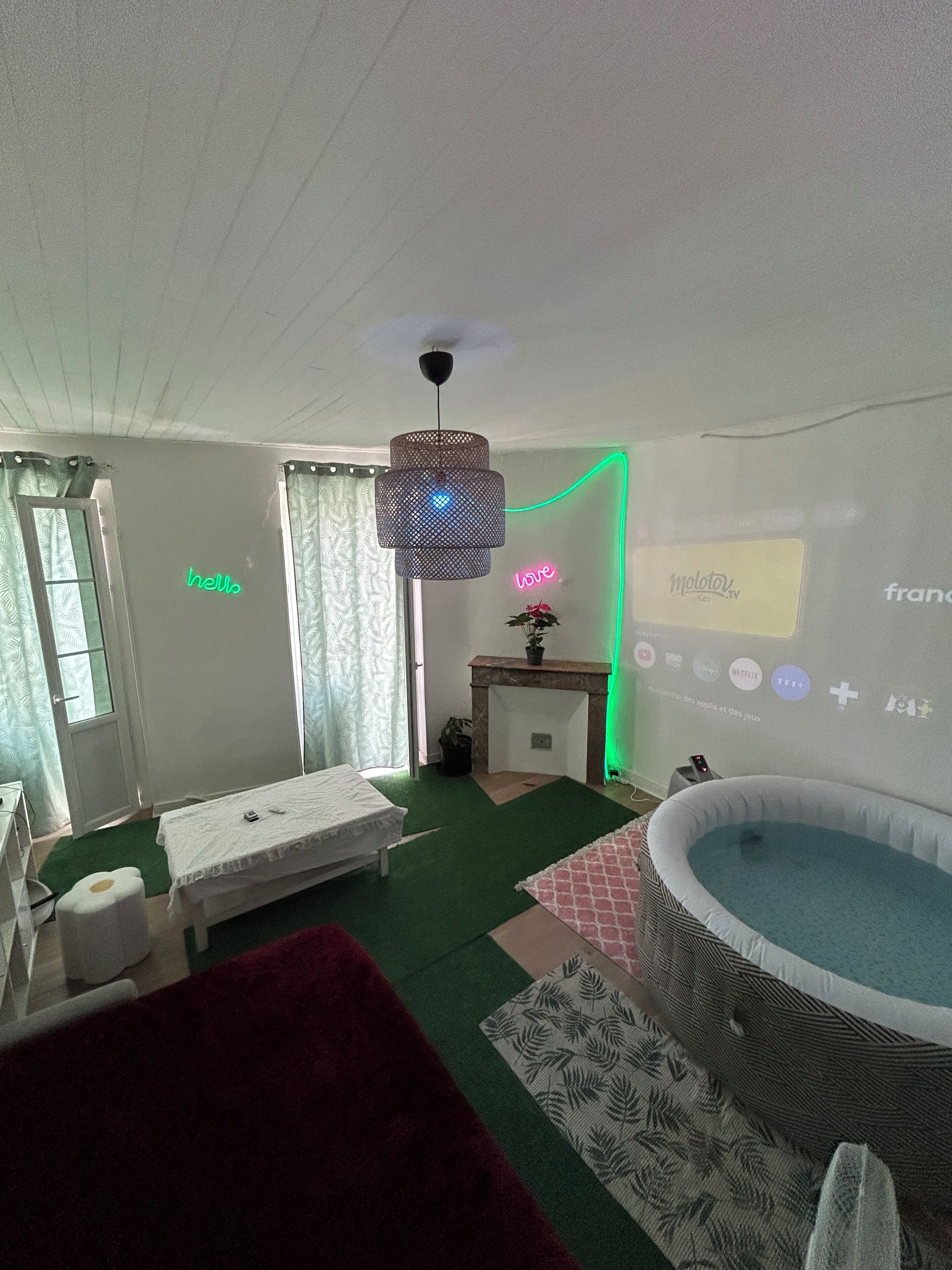 Une chambre avec un lit, une petite table, un écran de projection diffusant une chaîne de télévision et une piscine.