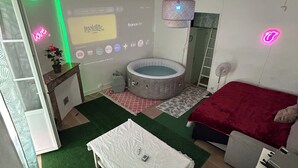 Une chambre avec un lit, une petite table, une chaise, un radiateur, un écran de projection et un panneau lumineux au néon.