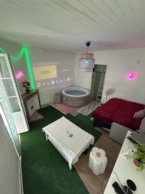 Ein Schlafzimmer mit einem Bett, einem kleinen Tisch, einem Stuhl, einem Heizgerät, einer Projektionsleinwand und einer Neonreklame.
