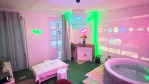 Une pièce comprenant un lit, une petite table, une plante, une fenêtre et un mur servant d’écran de projection.