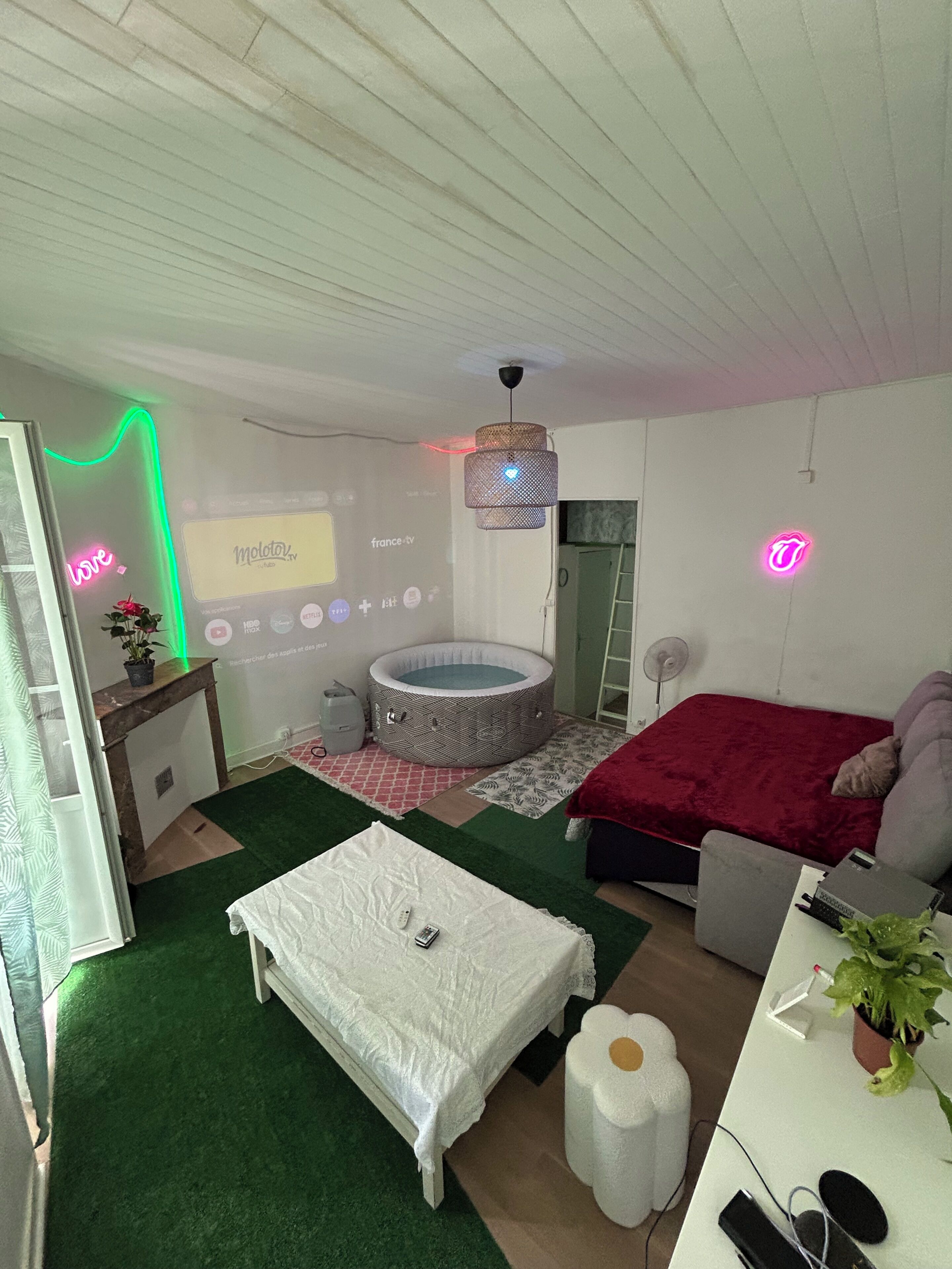 Un dormitorio con cama, una mesita, una silla, un escritorio, una pantalla para proyector, un jacuzzi y un ventilador de techo.