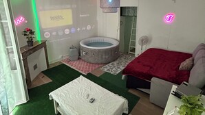 Une chambre à coucher comprenant un lit, une petite table, une chaise, un bureau, un écran de projection, un jacuzzi et un ventilateur de plafond.