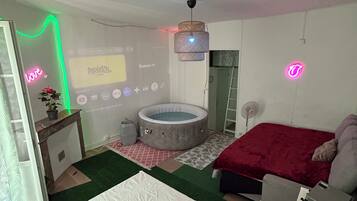 Un dormitorio con cama, una mesita, una silla, un escritorio, una pantalla para proyector, un jacuzzi y un ventilador de techo.