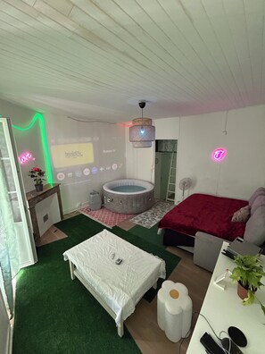 Ein Schlafzimmer mit Bett, kleinem Tisch, Stuhl, Schreibtisch, Projektionsleinwand, Whirlpool und Deckenventilator.