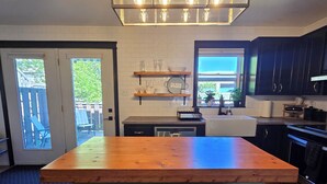 Una cocina con una isla de madera, dos taburetes de bar, una lámpara colgante y un ventanal con vistas.