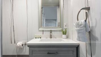 A bathroom with a marble wall, a sink with a mirror, a towel rack, and a plant.