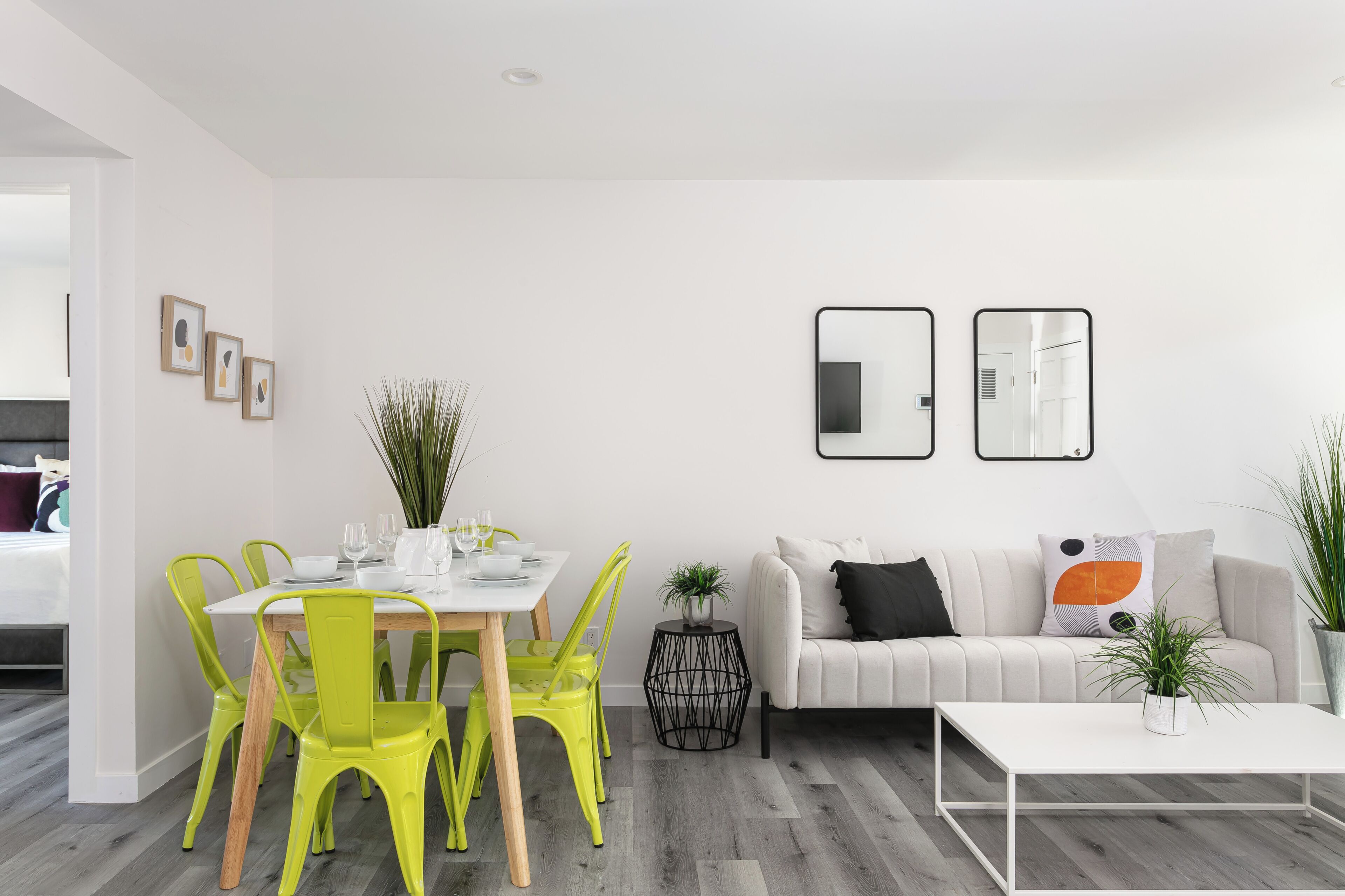 Uma sala de estar moderna com área de jantar, paredes brancas e chão de madeira cinza.