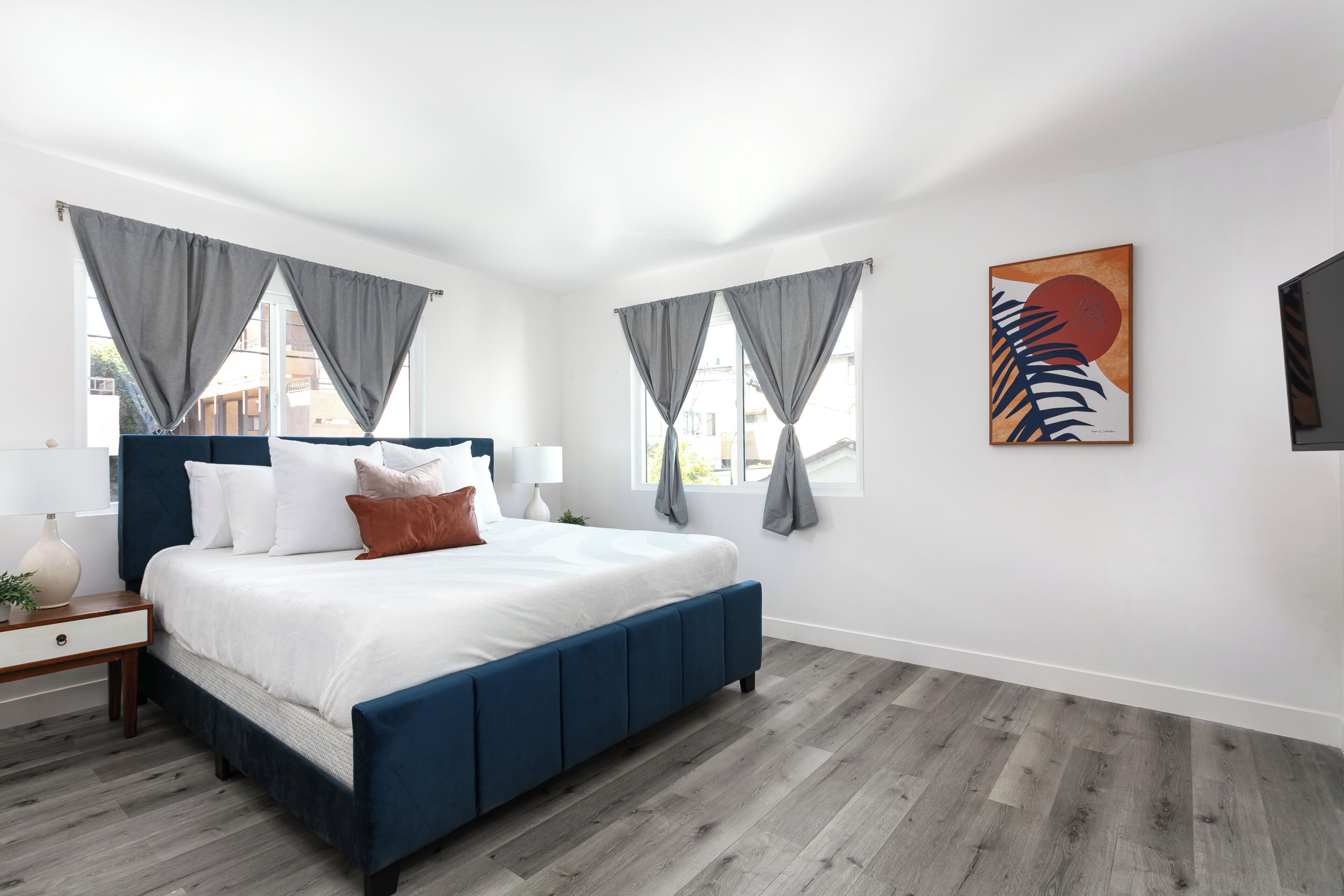 Een slaapkamer met een bed, gordijnen, een schilderij en een televisie.