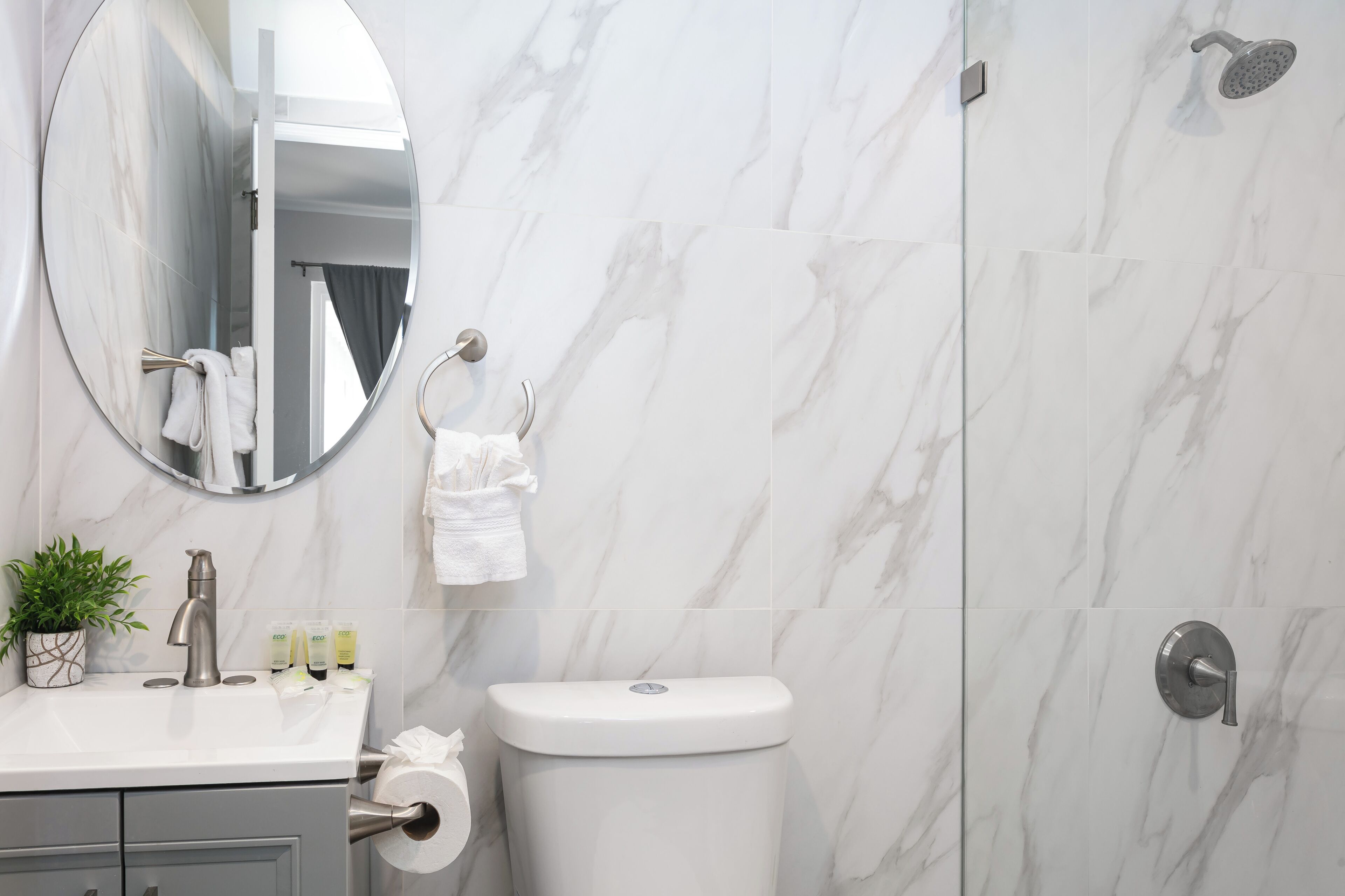 A bathroom with a marble wall, a round mirror, a toilet, and a shower area.