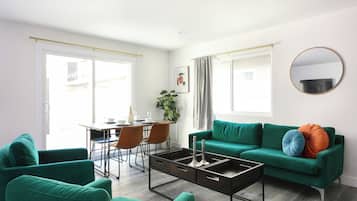 Un salon moderne avec un canapé vert, une table basse et un coin repas comprenant des chaises et une table.