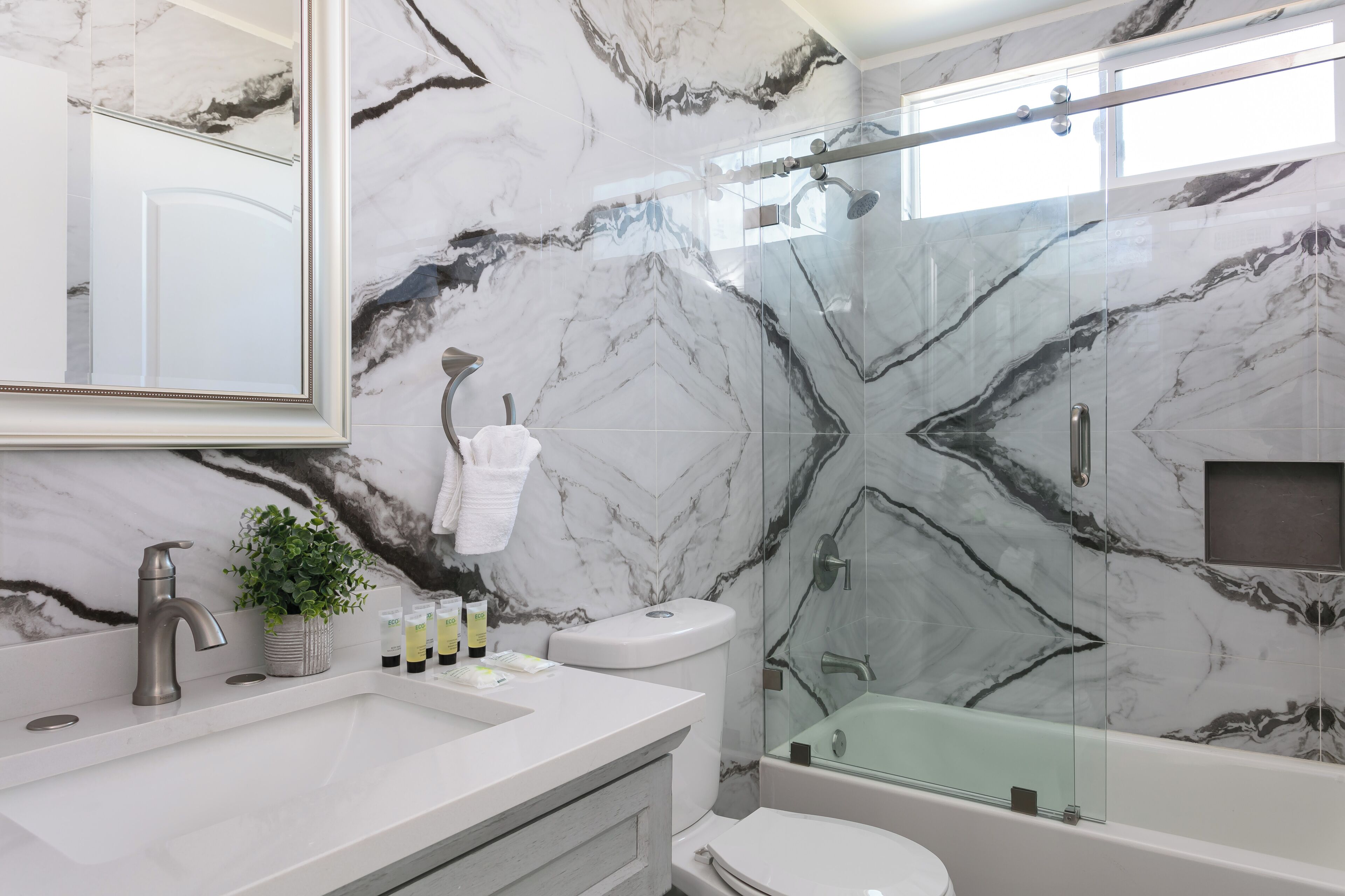 Een badkamer met een marmeren wand, een douche met glazen wanden, een witte wastafel en een toilet.