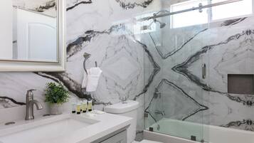 Een badkamer met een marmeren wand, een douche met glazen wanden, een witte wastafel en een toilet.