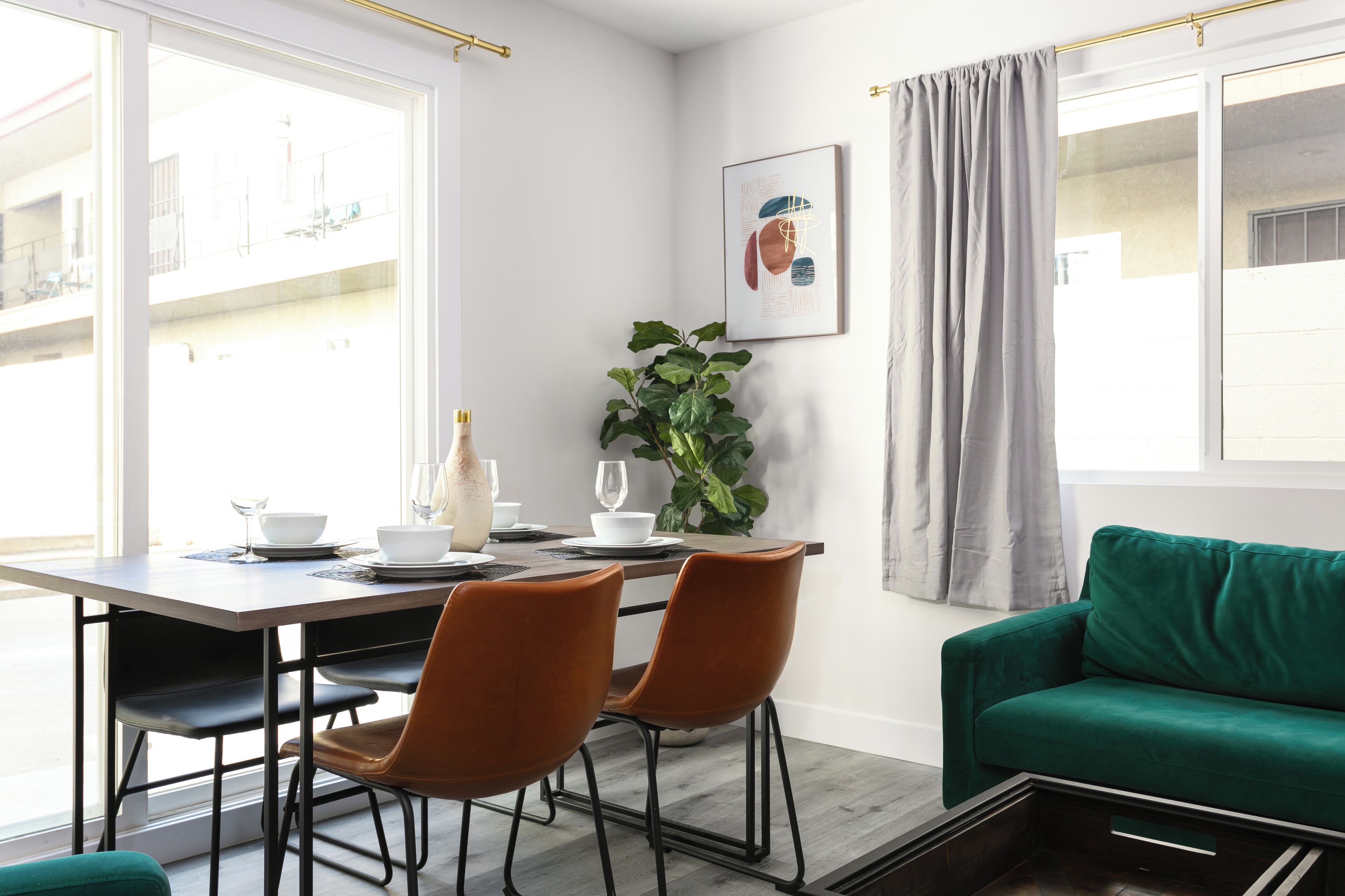 A dining area with a table set for two, a green sofa, and a potted plant.