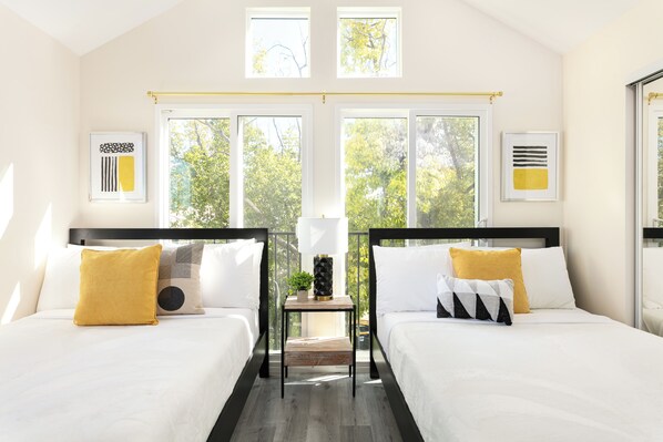 A room with two beds, a small table, and large windows with a view of trees. - Chic City Apt Near Americana Glendale (Glendale)
