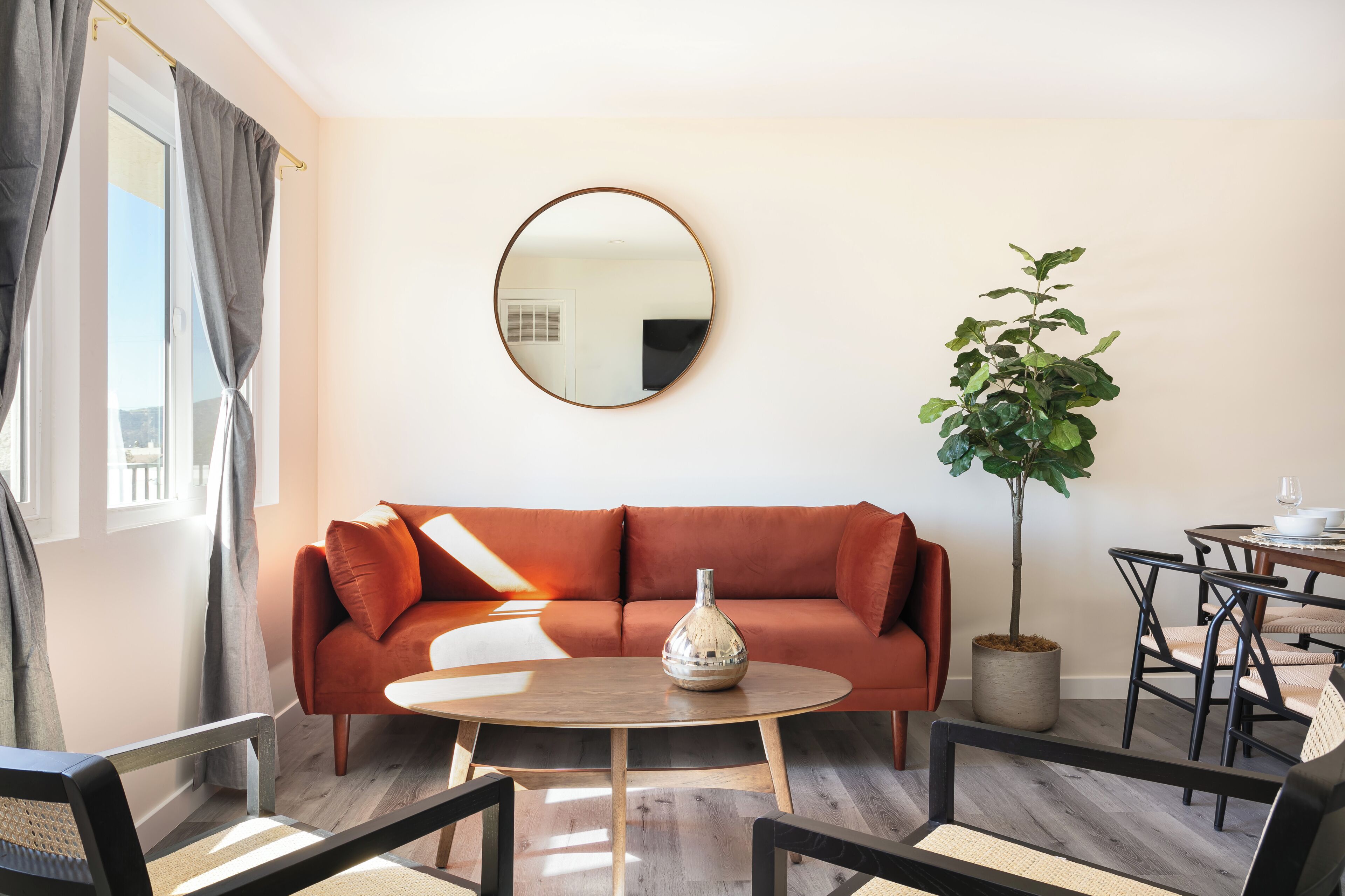 A living room with a sofa, round table, chairs, a potted plant, and a mirror on the wall.