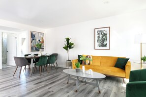 A modern living room with a dining area, a sofa, a coffee table, and a plant. - Chic City Apt Near Americana Glendale (Glendale)