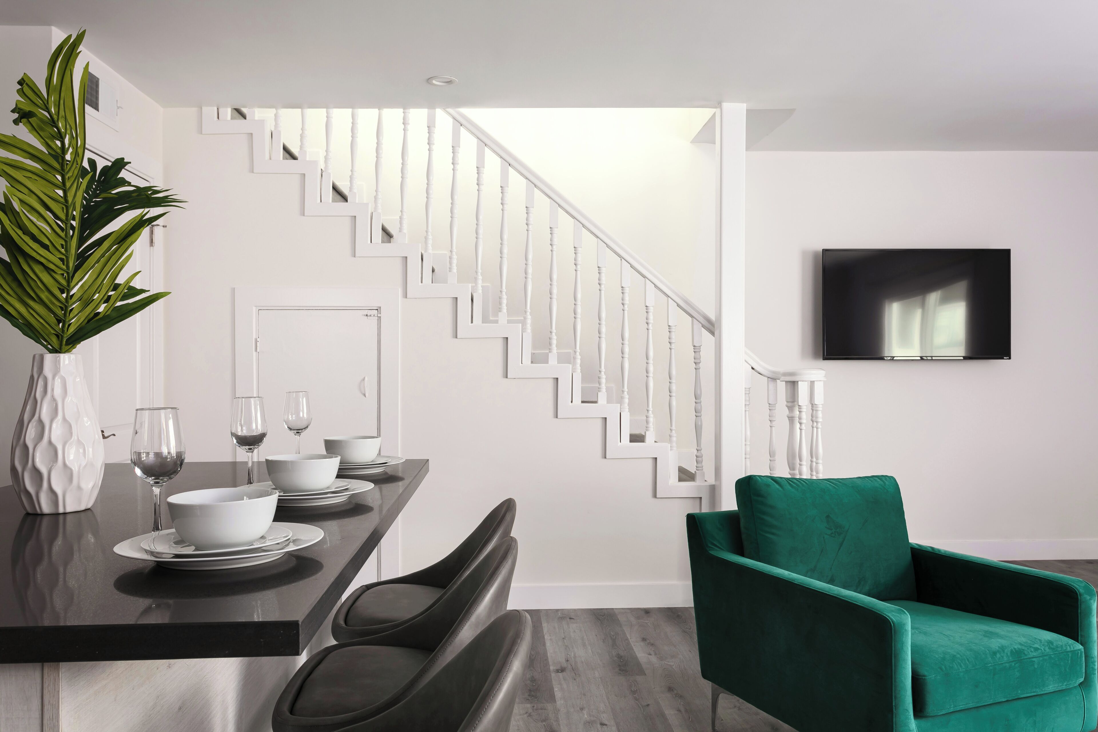 A modern dining area with a staircase, a flat-screen TV, and a green armchair.