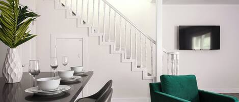 A modern dining area with a staircase, a flat-screen TV, and a green armchair.