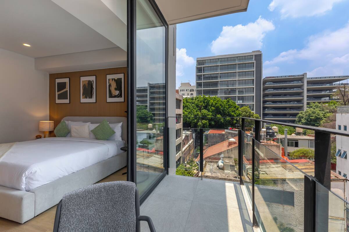 Una habitación de hotel moderna con una cama grande, un balcón de vidrio y vistas a la ciudad.