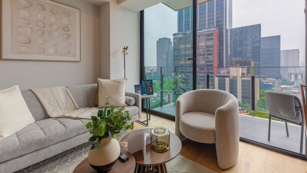Un salon moderne avec un canapé gris, une table basse ronde, un fauteuil gris et une grande fenêtre donnant sur la ville.