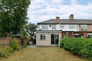 A two-story residential house with a front garden, a satellite dish, and a brick wall.