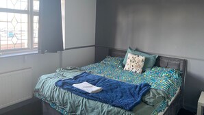 A bedroom with a bed, a window with curtains, a radiator, and a bedside table. - super king size bed room with cozy and big bed for 3 in fmaily home (Hornchurch)