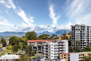 Ein mehrstöckiges Gebäude mit Balkonen, umgeben von Grünflächen und Bergen im Hintergrund.