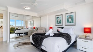 A modern bedroom with a large bed, a ceiling fan, a red lamp, and artwork on the wall. - The Surf Breeze Retreat (Coolangatta)