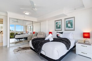 Um quarto moderno com uma cama grande, um ventilador de teto, uma luminária vermelha e obras de arte na parede.