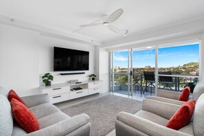 Uma sala de estar moderna com televisão de tela plana, ventilador de teto, varanda com mesa e cadeiras e vista para a cidade.