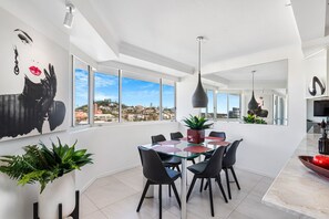 Uma zona de refeições moderna com mesa de vidro, cadeiras pretas e vista para a cidade.