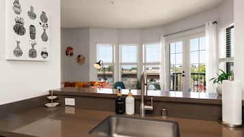 A modern kitchen with a stainless steel sink, a countertop with a bottle of hand soap, and a window overlooking a balcony.