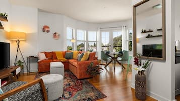 A modern living room with a sectional sofa, a dining table with chairs, a TV, and a large mirror.