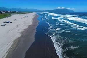 Uma praia com uma extensa faixa de areia, ondas quebrando na costa e um céu claro.